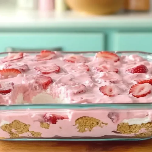 Glass dish of no-bake strawberry delight with a pink creamy layer, graham cracker crust, and fresh strawberry slices on top.