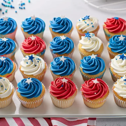 Red White and Blue Cupcakes—overhead view of 24 vanilla cupcakes topped with red, white, and blue buttercream swirls and star sprinkles, arranged neatly on a serving tray.