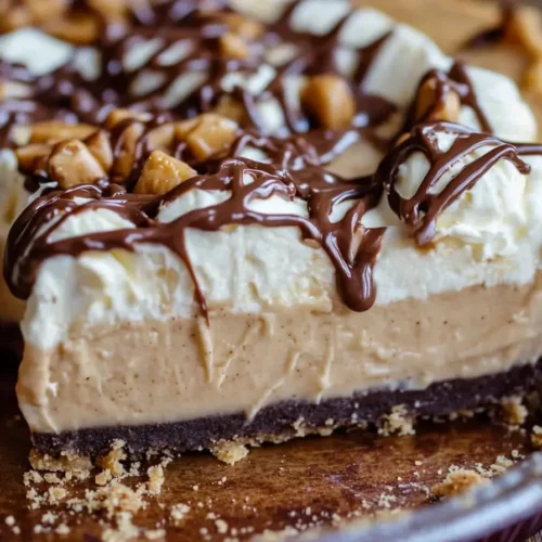Close-up of No-Bake Peanut Butter Pie: creamy layers, whipped cream, chocolate drizzle, and peanuts.