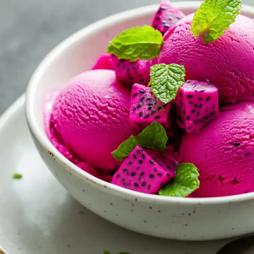 Dragon fruit ice cream in a white ceramic bowl, topped with fresh dragon fruit cubes and mint leaves, on a bright tropical background.